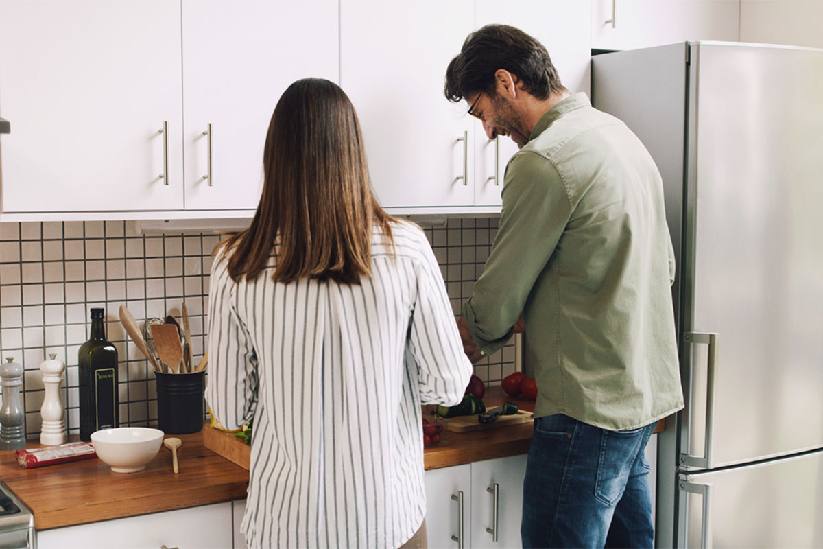 Man and women preparing food in a white kitchen with wooden worktop